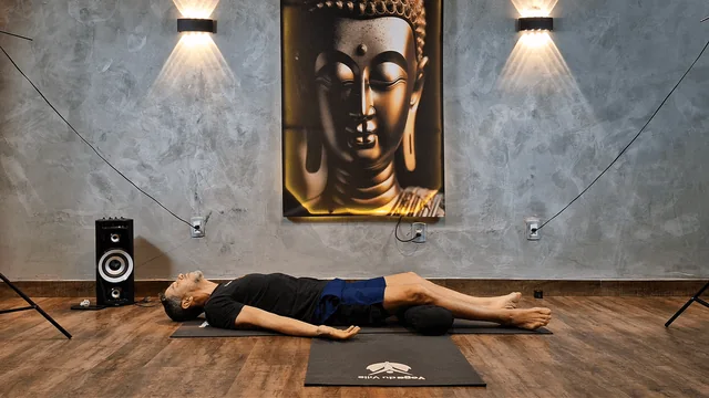 Praticante deitado de costas no tapete com braços ao lado do corpo e pernas estendidas em Savasana.